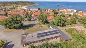 An aerial view of a coastal town with red-roofed buildings, a marina, and a large building with solar panels.