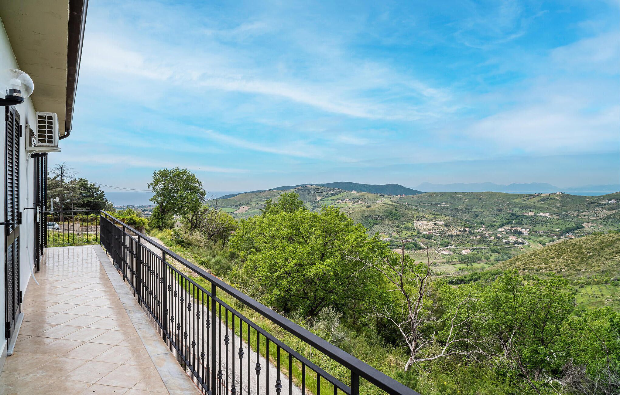 A balcony with a view of a green landscape and distant hills.