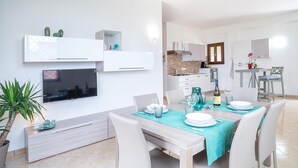 A modern living room with a flat-screen TV, a dining area with a table set for four, and a kitchen in the background. - Lovely home in Laureana Cilento (Laureana Cilento)
