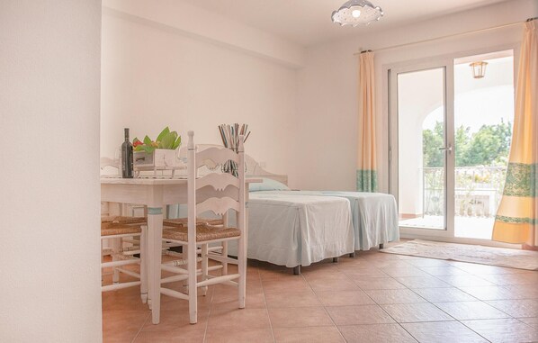 Une chambre avec deux lits, une table à manger avec des chaises et un balcon avec des rideaux.