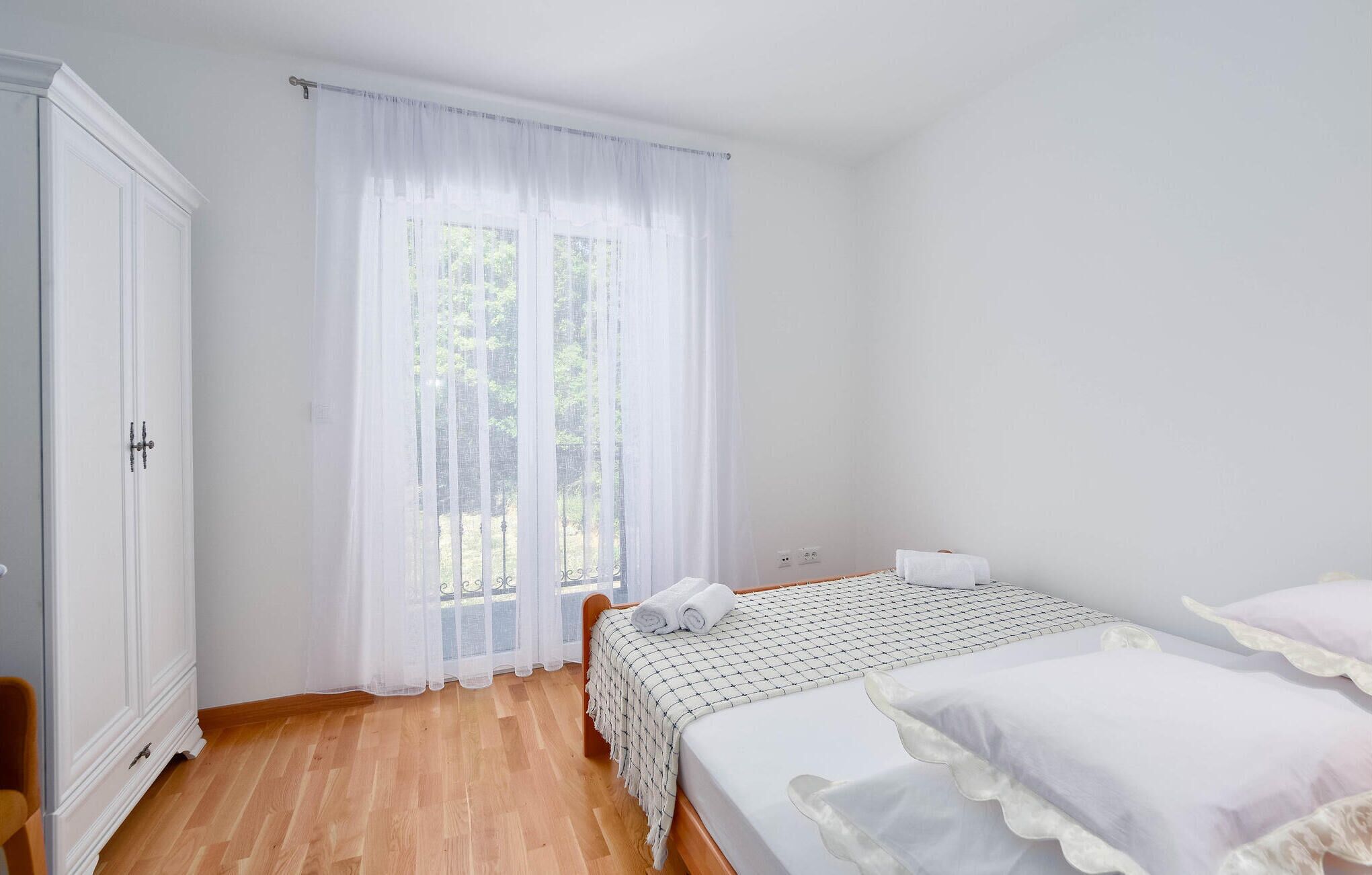 Une chambre à coucher avec un lit, une armoire et une fenêtre ornée de rideaux légers.