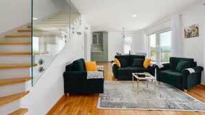 A modern living room with a staircase, two dark green sofas, a patterned rug, and a kitchen in the background. - Stunning home in Sinj (Sinj)