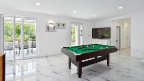 A modern living room with a pool table, a flat-screen TV, and a balcony with outdoor seating. - Stunning home in Sinj (Sinj)
