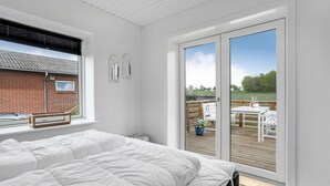 A bedroom with a large bed, a window, and a sliding glass door leading to an outdoor deck with a table and chairs. - 1 bedroom nice home in Rønne (Rønne)