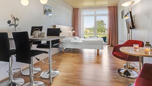 Quarto moderno com cama, mesa de jantar com cadeiras, uma cadeira vermelha e vista para o exterior.