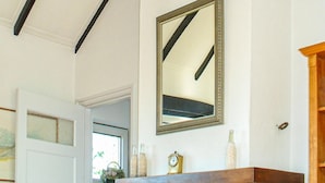 Une pièce avec une cheminée en bois, un miroir, une horloge et une fenêtre donnant sur un paysage verdoyant.