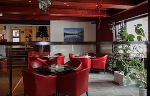 Um restaurante com cadeiras e mesas vermelhas, uma janela grande com plantas e um quadro na parede.