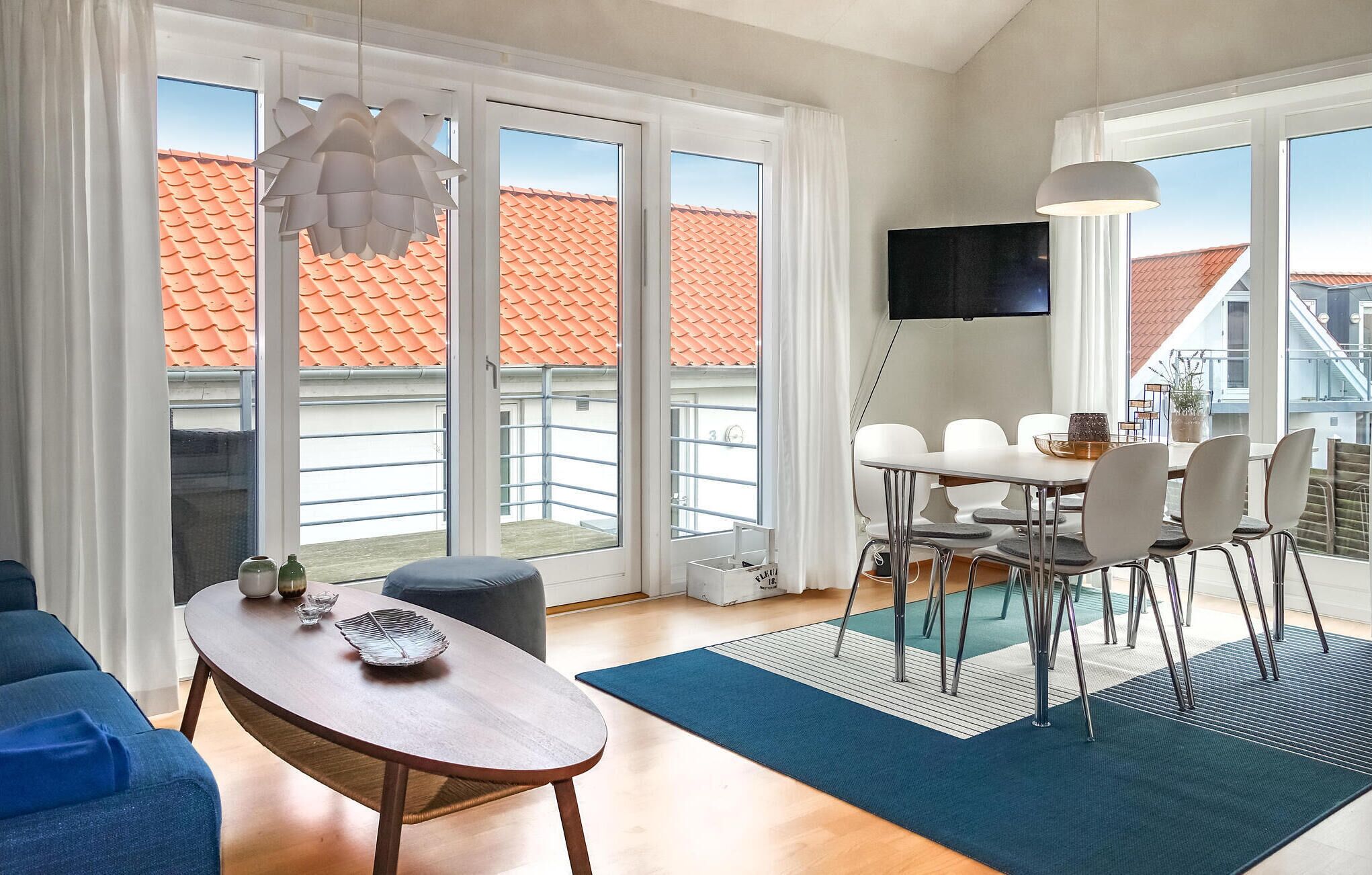 A modern living room with a wooden table, blue sofa, and a dining area with white chairs.