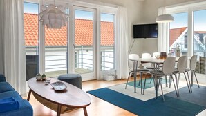Ein modernes Wohnzimmer mit Holztisch, blauem Sofa und einer Essecke mit weißen Stühlen.