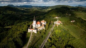 Ein Luftbild eines Schlosses mit einer Kirche, umgeben von üppigen grünen Hügeln und einer gewundenen Straße.