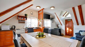 Eine kompakte Küche mit Mikrowelle, Herd und Spüle, ein Essbereich mit Tisch und Stühlen sowie ein Wohnbereich mit Sofa und Fernseher.