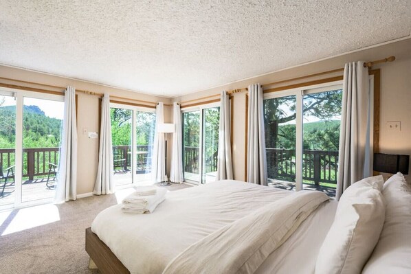 Un dormitorio espacioso con una cama grande, puertas de vidrio correderas que dan a una terraza exterior y vistas a zonas verdes.