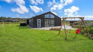 Ett modernt hus med ett stort fönster och en gunga i trädgården.