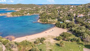 Eine Luftaufnahme einer Küstenregion mit Strand, klarem, blauem Wasser und dichter umliegender Vegetation.