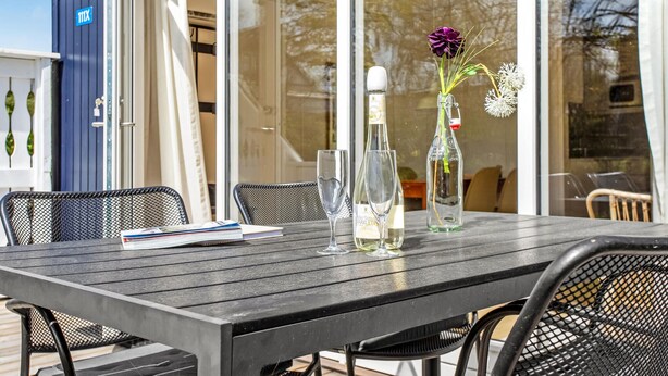 A wooden table with two wine glasses, a bottle of Sparklettner, and a vase with flowers. - Amazing home in Gudhjem with WiFi (Gudhjem)