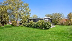 A single-story mobile home with a dark exterior, surrounded by a well-maintained lawn and various trees. - Amazing home in Gudhjem with WiFi (Gudhjem)