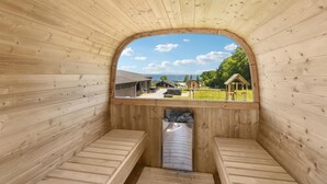 Een sauna met houten wanden en banken, met uitzicht op een erf met een klein houten gebouw en een heldere lucht.