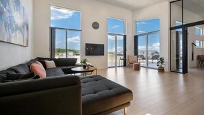 Een ruime woonkamer met een donkergrijze bank, een ronde salontafel en een groot raam met uitzicht op de omgeving.