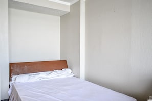 A small, simple room with a single bed, plain walls, and a plain ceiling.