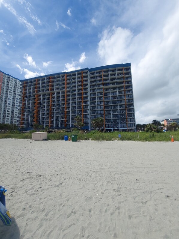 A large, multi-story hotel with a modern design, featuring numerous balconies and a prominent orange structural element.