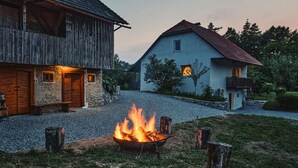 En rustik lade og et moderne hus med grusindkørsel og et bålsted i forgrunden.
