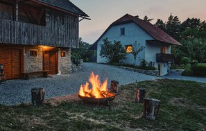 A rustic barn and a modern house with a gravel driveway and a fire pit in the foreground.