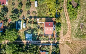 Vista aérea de uma área residencial com piscina, casa com telhado vermelho e vegetação ao redor.