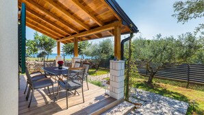 Un patio al aire libre con una pérgola de madera, pilares de piedra y una mesa con sillas.