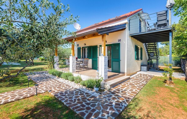 Uma casa de dois andares com telhado de telhas vermelhas, persianas verdes e entrada com calçada de pedra.