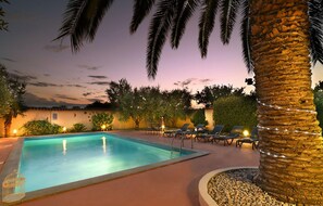 A swimming pool with lounge chairs and palm trees, surrounded by a stone wall and vegetation. - Gorgeous home in Pula (Pula)