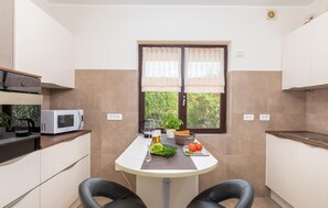 A compact kitchen with a dining table, two chairs, a microwave, a kettle, and a window with curtains. - Gorgeous home in Pula (Pula)
