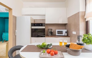 A compact kitchenette with a microwave, coffee maker, and oven. A dining table with a placemat, fresh vegetables, and a cutting board is in the foreground. - Gorgeous home in Pula (Pula)