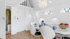 Un comedor moderno con mobiliario blanco, una mesa de comedor de madera y un frutero.