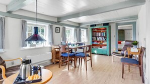 Una habitación acogedora con una mesa de madera, sillas, una estantería y una ventana con cortinas.