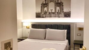 A neatly made bed with a pillow and a folded towel, a wall-mounted picture of a historical monument, and bedside lamps. - Room 5 - Double - B&B L'Infinito 88 Charmant Rooms (Napoli)