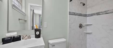 A bathroom with a white sink, a toilet, a shower with marble tiles, and a mirror.
