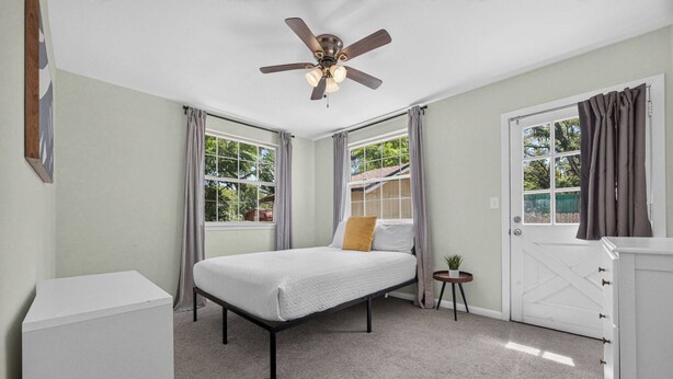 A bedroom with a bed, a ceiling fan, a door, and windows. - Pure GOLD on Emerald Isle - 4BR, Patio, WIFI (Jacksonville)