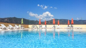 A swimming pool with lounge chairs and umbrellas, surrounded by mountains. - Nice apartment in Villasimius with WiFi (Villasimius)