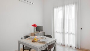 A dining area with a table set for two, a television on a cabinet, and a window with sheer curtains. - Nice apartment in Villasimius with WiFi (Villasimius)