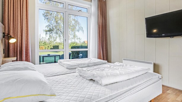 A bedroom with a bed, a TV, and a window with curtains.