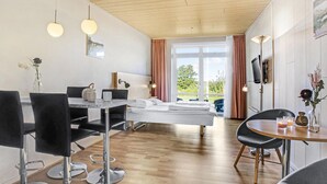 A hotel room with a bed, a dining table with chairs, a TV mounted on the wall, and a window with curtains.