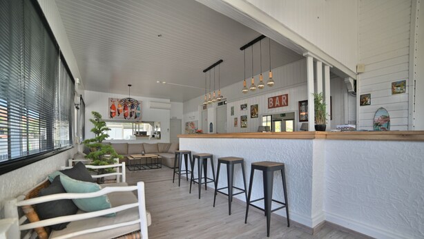 Un espace bar moderne avec un comptoir en bois, des tabourets de bar et un coin salon comprenant un canapé et un petit sapin de Noël.