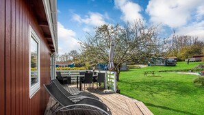 A wooden deck with outdoor furniture, a grassy lawn, and a tree.