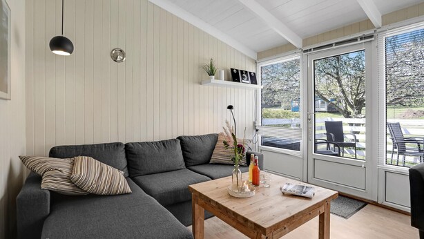 A modern living room with a grey sectional sofa, a wooden coffee table, and a large window offering a view of the outdoors.