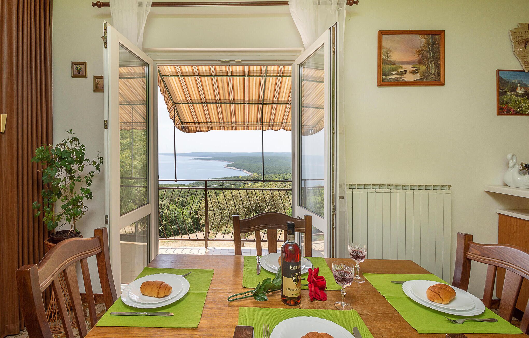 Comedor con mesa preparada para dos personas, una botella de vino y vista a un lago a través de amplios ventanales.