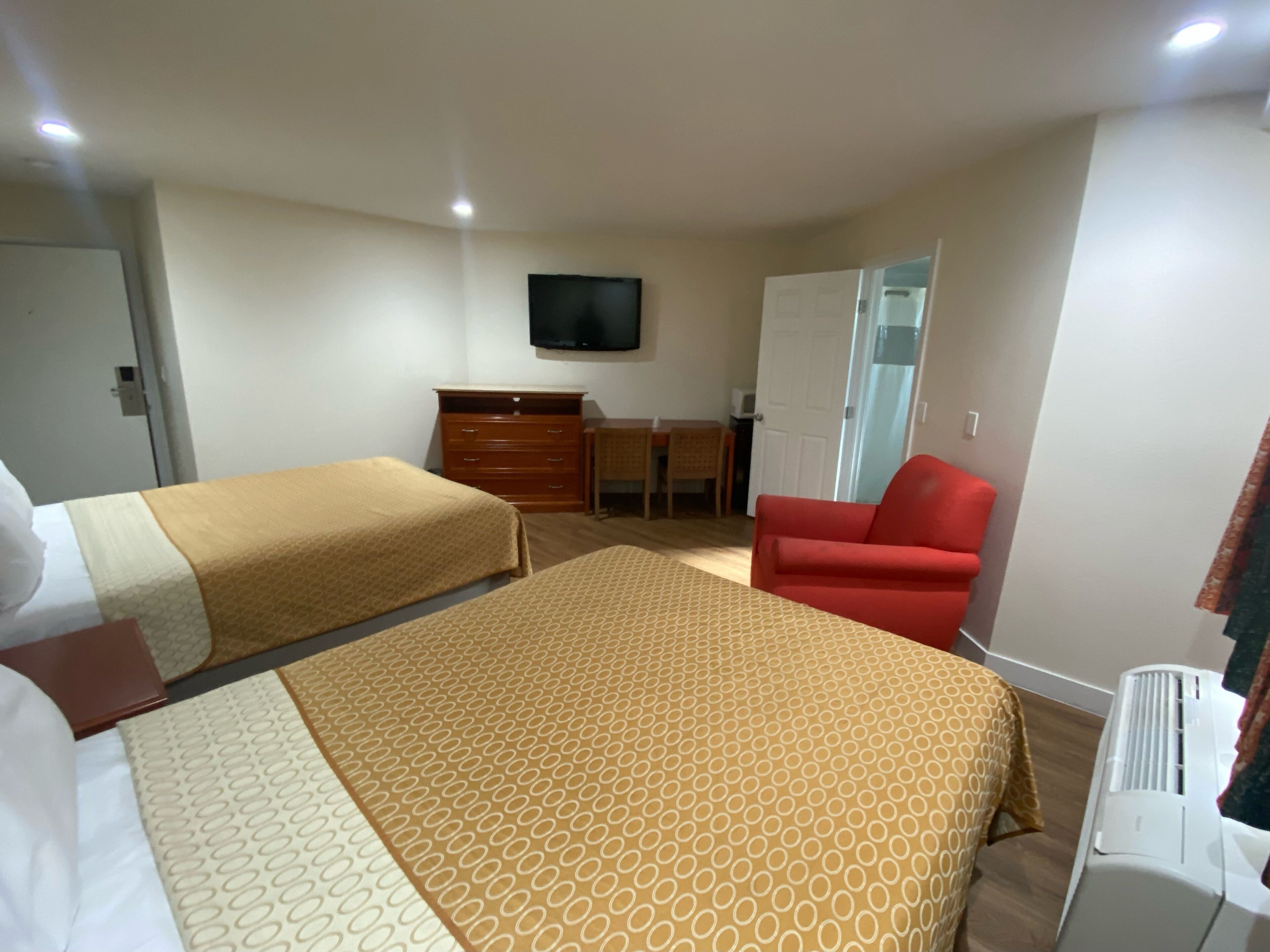 A hotel room with two beds, a desk, a chair, a television, and an air conditioning unit.
