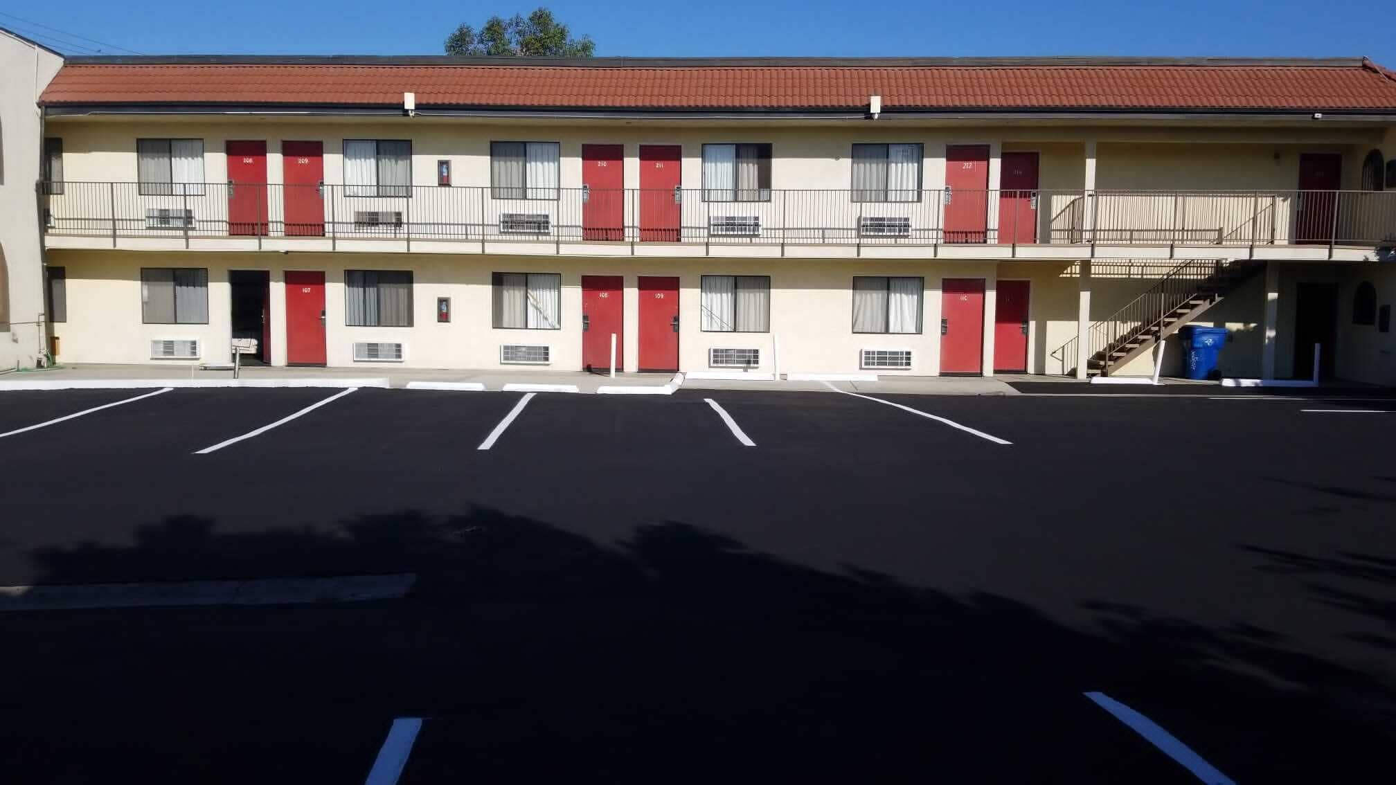 A motel with a two-story structure, multiple red doors, and a parking lot with marked spaces.