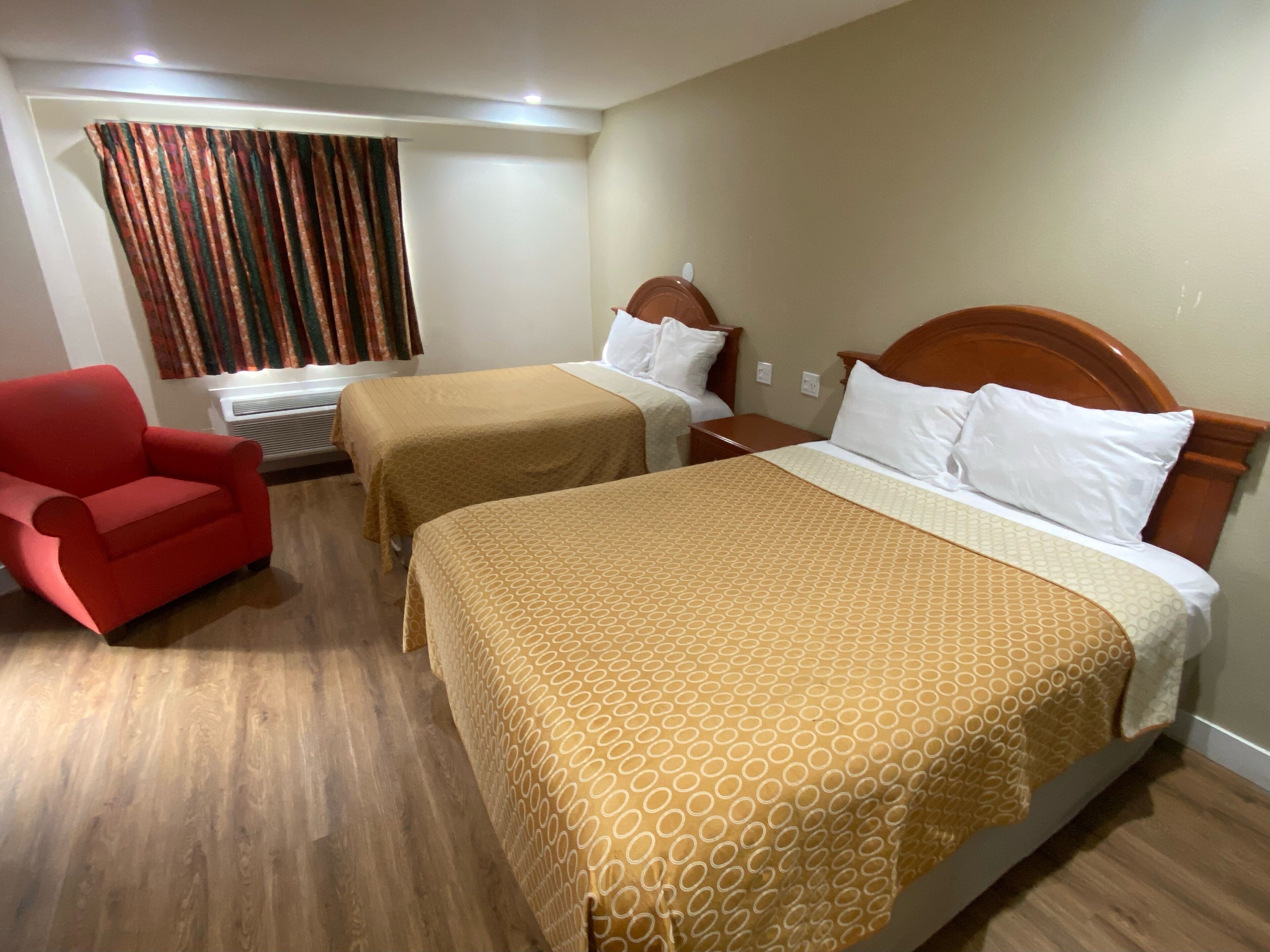 A hotel room with two beds, a red armchair, and a window with curtains.