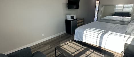 A bedroom with a bed, a TV, a microwave, and a small desk.