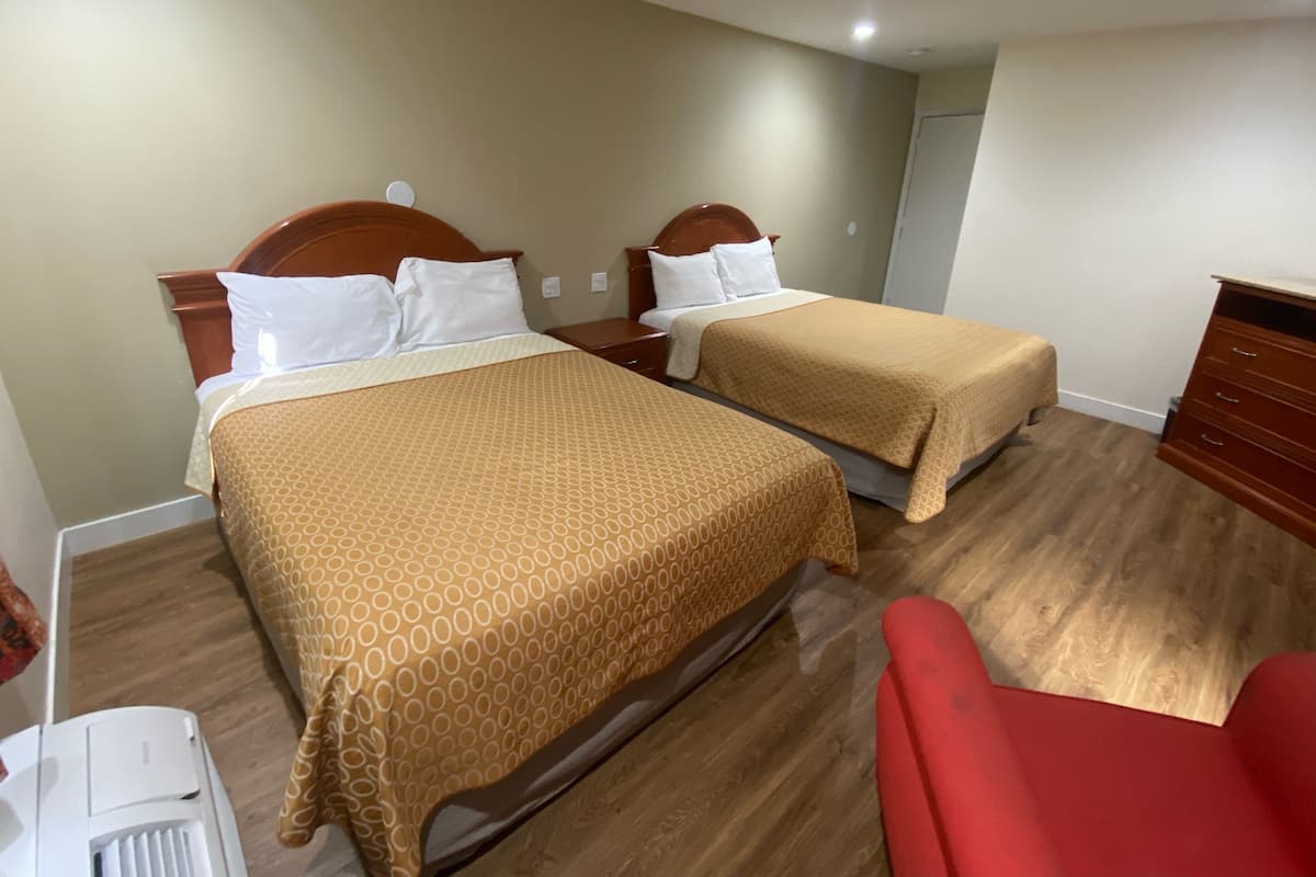 Hotellihuone, jossa on kaksi sänkyä, puiset päätyosat ja punainen tuoli.